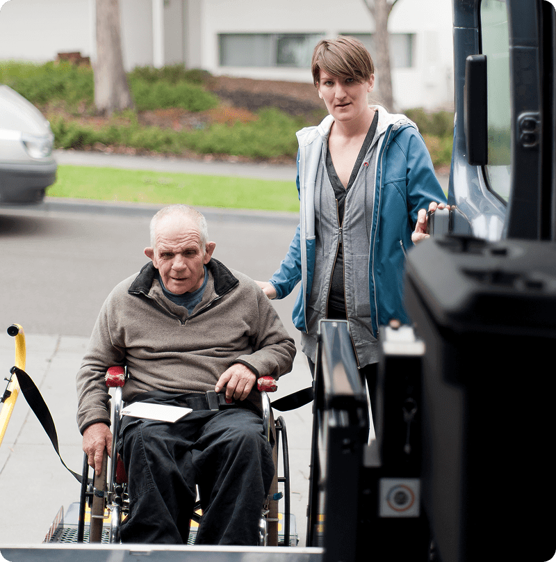 Man in wheelchair assisted onto vehicle lift.