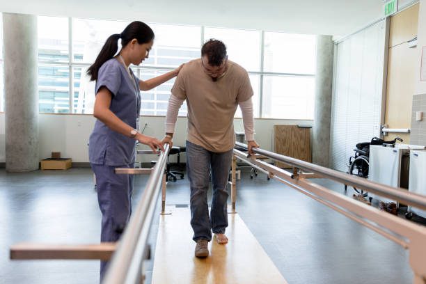 A man walking on some bars while being assisted by a nurse.